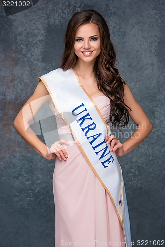 Image of Beautiful young brunette woman with her hair posing in a i long dress. Studio, on gray background