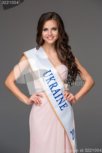 Image of Beautiful young brunette woman with her hair posing in a i pink dress. Studio, on gray background