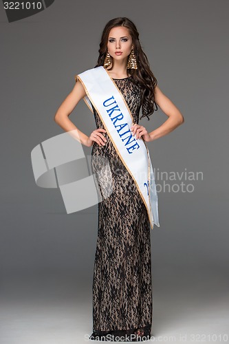 Image of Beautiful young brunette woman with her hair posing in a i long dress. Studio, on gray background