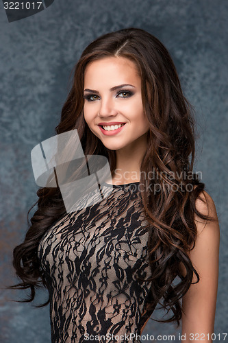 Image of Beautiful young brunette woman with her hair posing in a tracery dress. Studio, on gray background