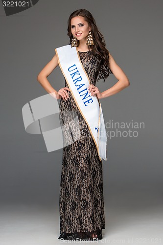 Image of Beautiful young brunette woman with her hair posing in a i long dress. Studio, on gray background