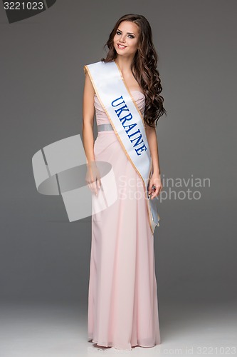 Image of Beautiful young brunette woman with her hair posing in a i long dress. Studio, on gray background