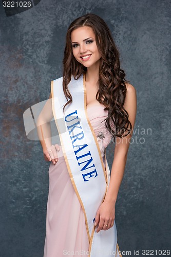 Image of Beautiful young brunette woman with her hair posing in a i pink dress. Studio, on gray background