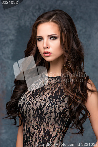 Image of Beautiful young brunette woman with her hair posing in a tracery dress. Studio, on gray background