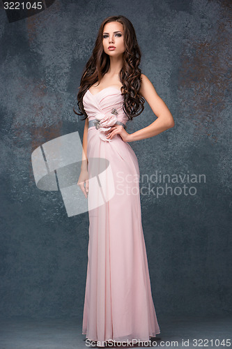 Image of Beautiful young brunette woman with her hair posing in a i long pink dress. Studio, on gray background