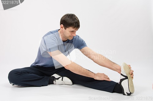 Image of The young man stretches muscles of left leg