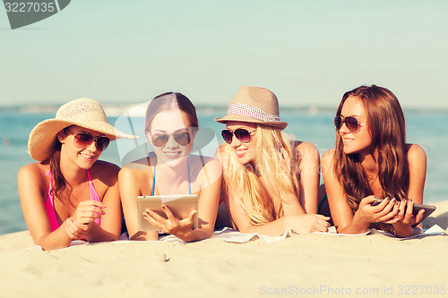 Image of group of smiling young women with tablets on beach