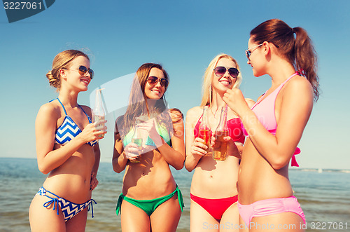 Image of group of smiling young women drinking on beach