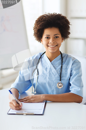 Image of happy female doctor or nurse writing to clipboard