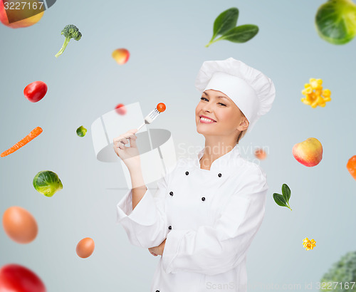 Image of smiling female chef with fork and tomato