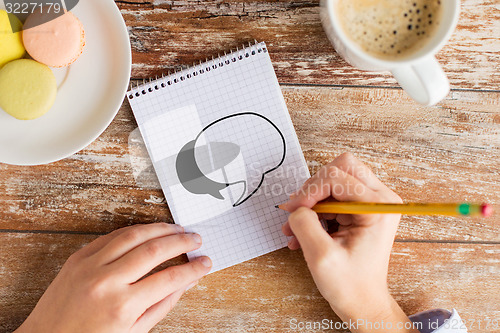 Image of close up of hands drawing text bubble to notebook