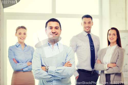 Image of smiling businessman in office with team on back