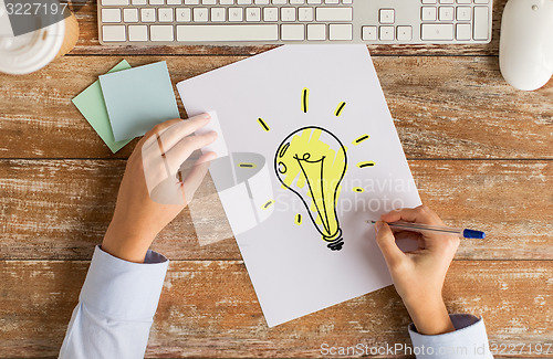 Image of close up of hands drawing ligting bulb on paper