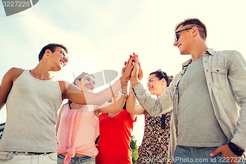 Image of group of smiling friends making high five outdoors