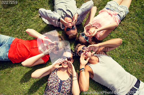 Image of group of smiling friends lying on grass outdoors