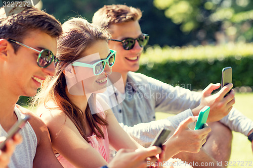 Image of smiling friends with smartphones sitting on grass