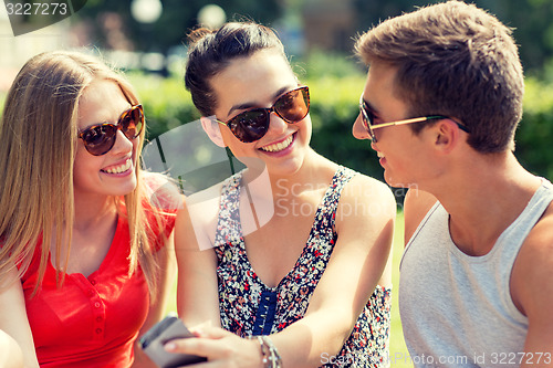 Image of smiling friends with smartphone sitting in park