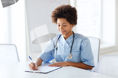 Image of happy female doctor or nurse writing to clipboard