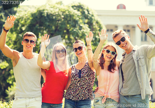 Image of group of smiling friends waving hands outdoors