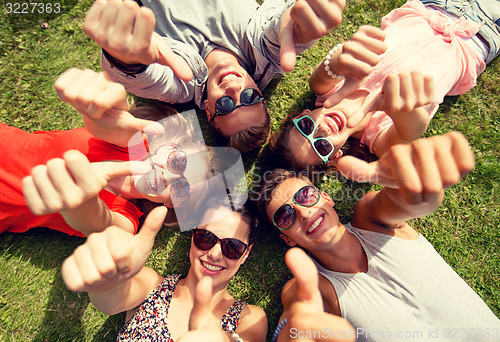 Image of smiling friends showing thumbs up lying on grass