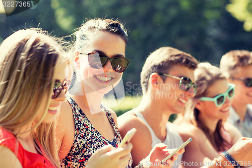 Image of smiling friends with smartphones sitting in park