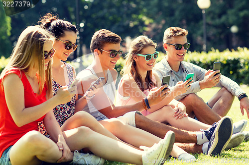 Image of smiling friends with smartphones sitting on grass