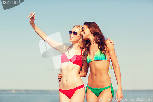 Image of two smiling women making selfie on beach