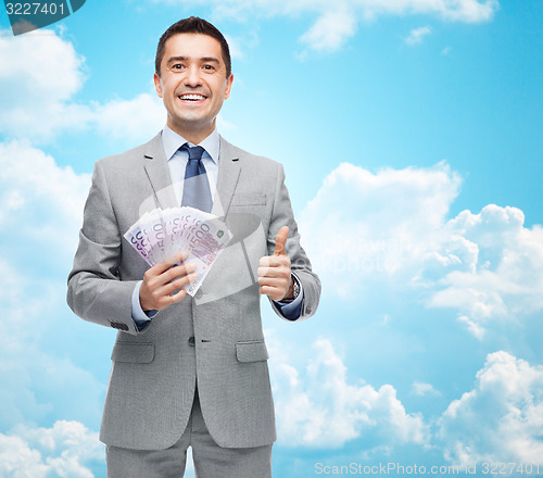 Image of smiling businessman with money showing thumbs up