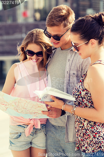 Image of smiling friends with map and city guide outdoors