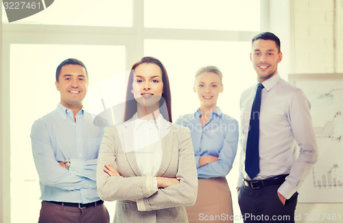 Image of smiling businesswoman in office with team on back