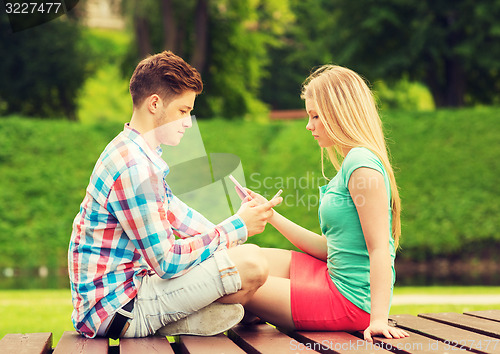 Image of couple with smartphones sitting on bench in park