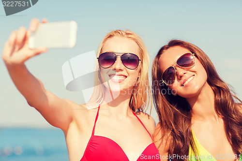 Image of two smiling women making selfie on beach