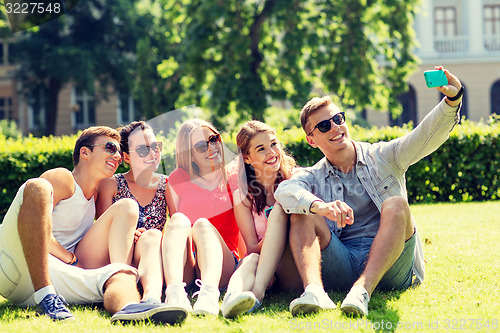 Image of smiling friends with smartphone sitting on grass