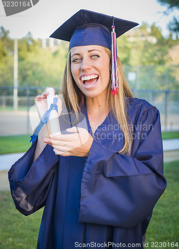 Image of Expressive Young Woman Holding Diploma in Cap and Gown