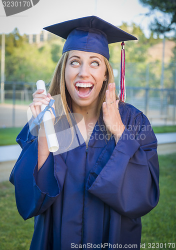 Image of Expressive Young Woman Holding Diploma in Cap and Gown