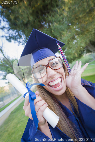 Image of Expressive Young Woman Holding Diploma in Cap and Gown