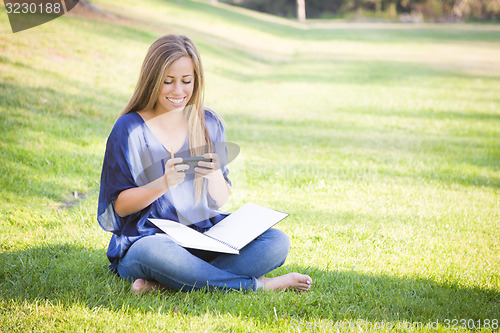 Image of Smiling Young Woman with Book and Cell Phone Outdoors