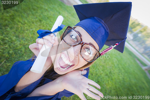 Image of Expressive Young Woman Holding Diploma in Cap and Gown