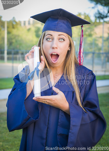 Image of Expressive Young Woman Holding Diploma in Cap and Gown