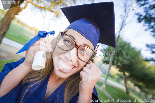 Image of Expressive Young Woman Holding Diploma in Cap and Gown