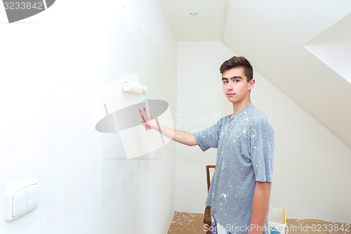 Image of teenager painting wall to white at home