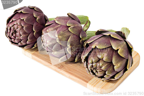 Image of Three artichokes on a wooden plate