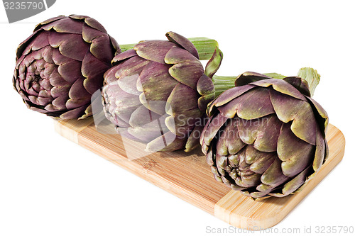 Image of Three artichokes on a wooden plate