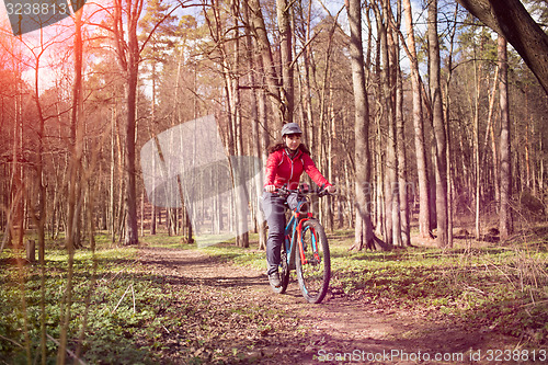 Image of Young woman riding a bicycle through forest