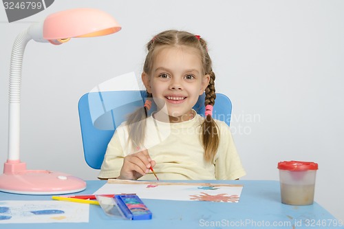 Image of Six year old girl smiling happily, drawing the table