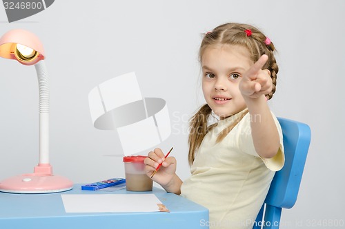 Image of Girl painting paints at table, points the finger