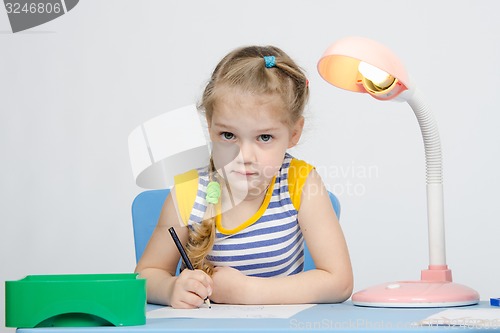 Image of Girl sits at the table and draws a blue pencil