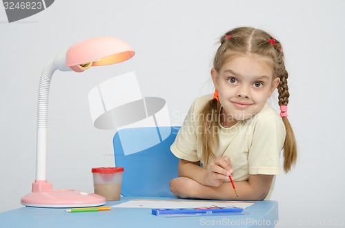 Image of Girl painting paints at the table, looked into frame