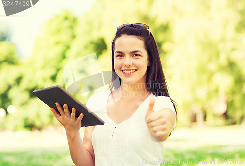 Image of smiling young girl with tablet pc sitting on grass
