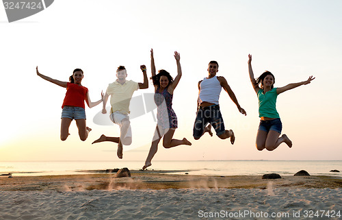 Image of smiling friends dancing and jumping on beach